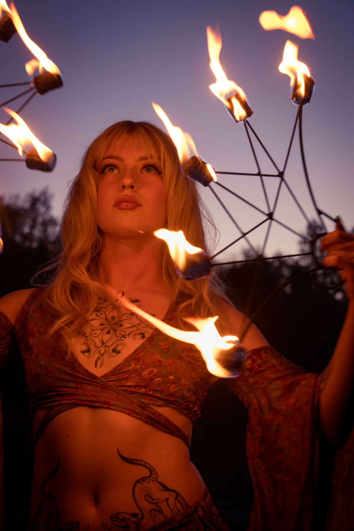 Portrait of a performer lit by fire fans against a violet sky