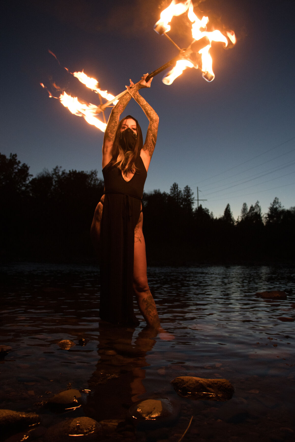 Silhouetted performer holding a flaming staff overhead at blue hour