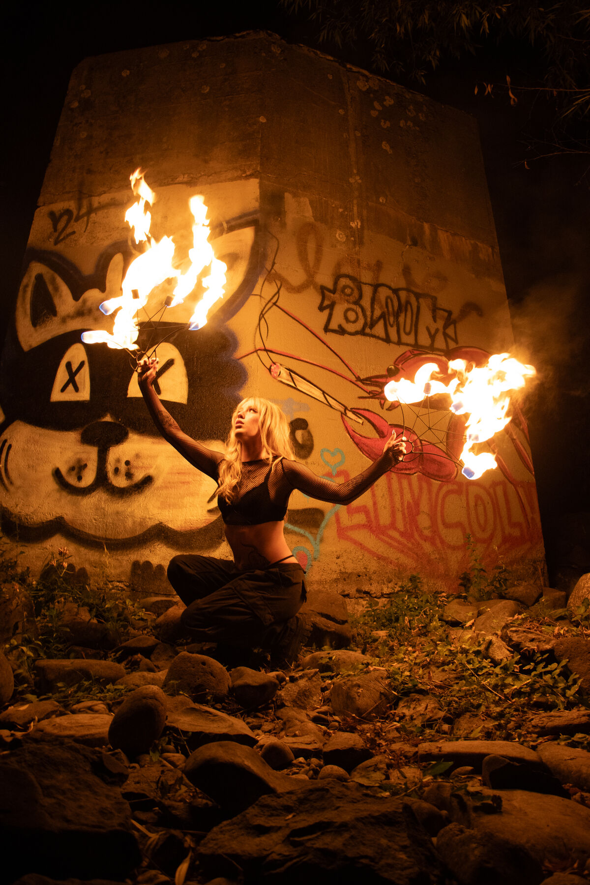 Fire performer kneeling in front of a painted concrete wall