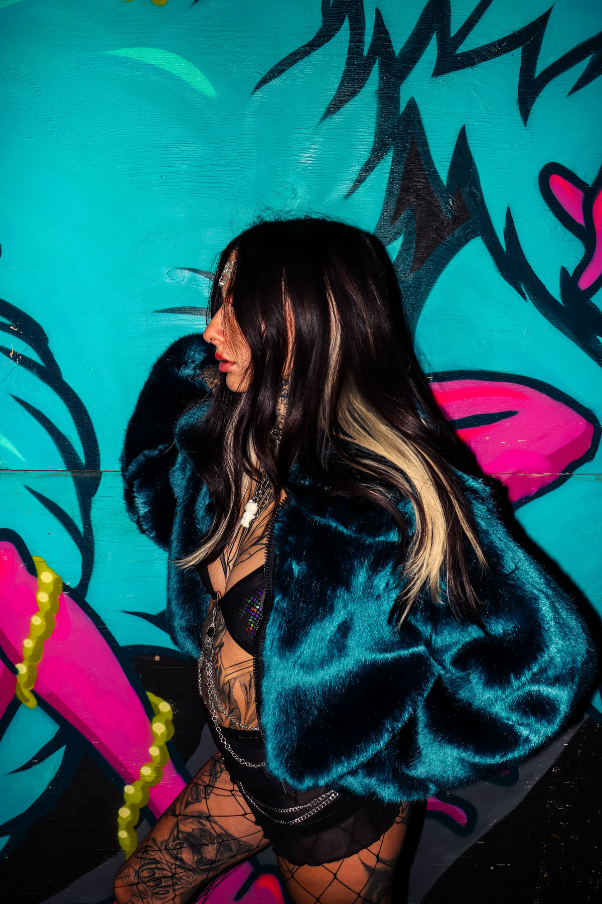Profile of the dark green faux fur coat against a teal mural