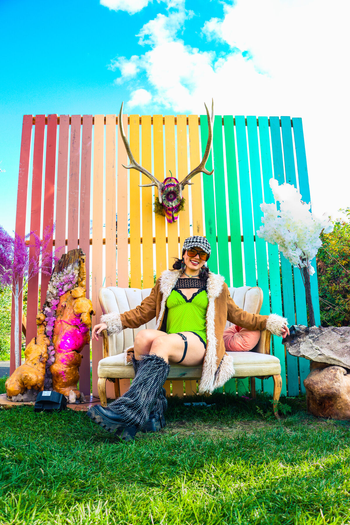 Festival goer lounging on a vintage sofa in front of a rainbow painted fence