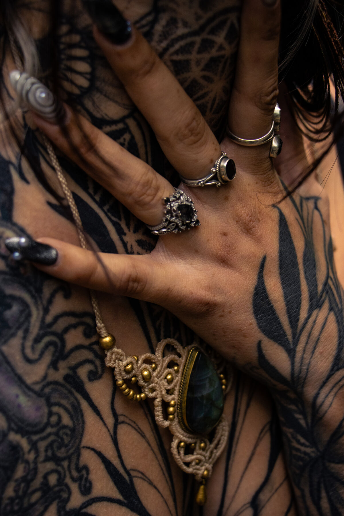 Detail of a tattooed hand with silver rings and a gold pendant